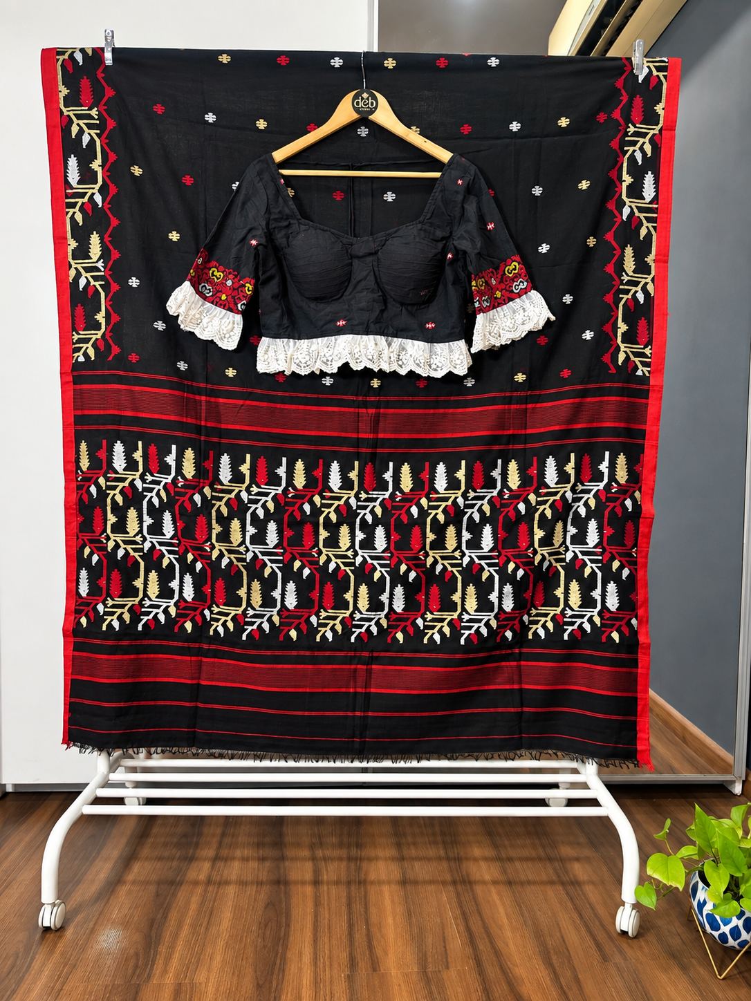 Black Jamdani saree with a red border and red, white and gold motifs, styled with a black blouse with lace frills on a Deb Looms hanger